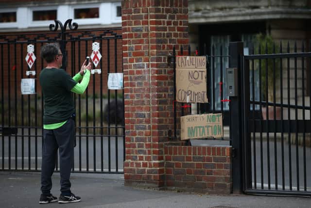 A pedestrian takes a photo of a placards saying ‘catcalling is not a compliment’ and ‘a skirt is not an invitation’ attached to the fence outside James Allen’s Girls’ School (JAGS) on March 28, 2021 in London, England. Credit: Hollie Adams/Getty Images