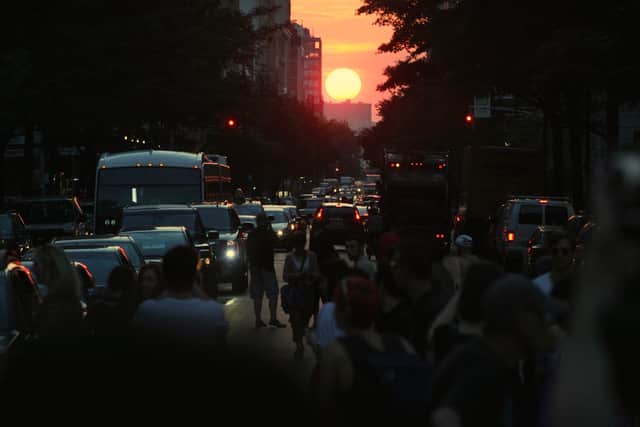 People watch and photograph the sunset on 14th Street during Manhattanhenge - Credit: Getty