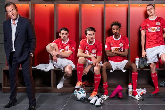 Will Arnett as Mark Crane, Jack McMullen as Jack Turner, Jake Short as Mattie Sullivan, Jake Short as Mattie Sullivan, Shaquille Ali-Yebuah as Benji Achebe, and Theo Barklem-Biggs as Petey Brooks in The First Team, wearing red football kits in the locker room (Credit: BBC Two)