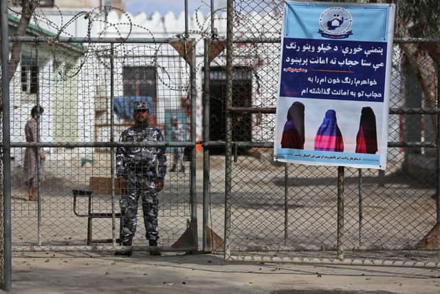A Taliban prison security guard stands next to a poster ordering women to cover themselves with a Hijab during the distribution of new uniforms' ceremony by the Taliban authorities at a prison in Jalalabad on February 5, 2023. (Photo by Shafiullah KAKAR / AFP) (Photo by SHAFIULLAH KAKAR/AFP via Getty Images)