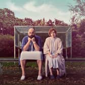 Youssef Kerkour as Sam and Katherine Parkinson as Anna in Significant Other, wearing hospital gowns and sat on a park bench (Credit: ITV)