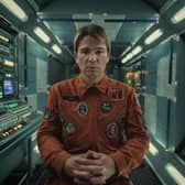 Josh Hartnett as David Ross in Black Mirror 6x3 Beyond the Sea, wearing an orange jumpsuit and sitting in a spaceship, surrounded by switches and dials (Credit: Nick Wall/Netflix)