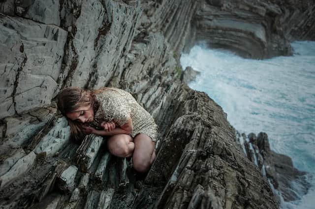 A young woman crouches on the rockface next to the sea in Spiral of Lies (Credit: Walter Presents)