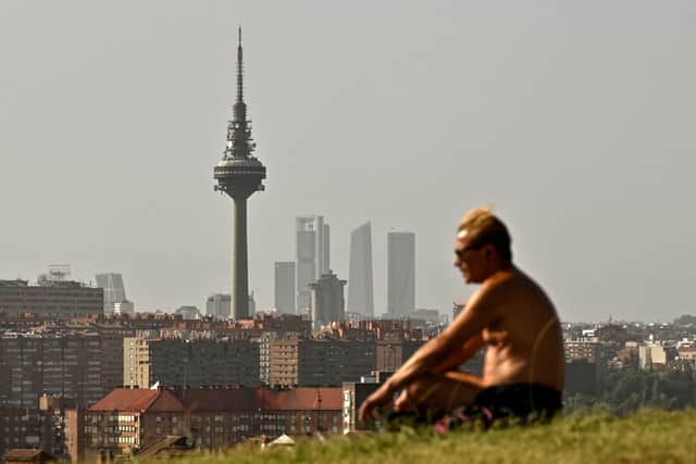 A man sits in a park in Madrid skyline during the heat wave in Madrid on 19 July (Photo by OSCAR DEL POZO/AFP via Getty Images)