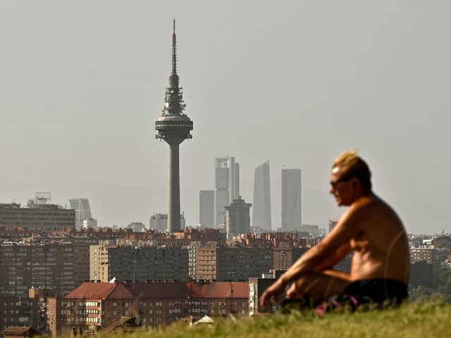 A man sits in a park in Madrid skyline during the heat wave in Madrid on 19 July (Photo by OSCAR DEL POZO/AFP via Getty Images)