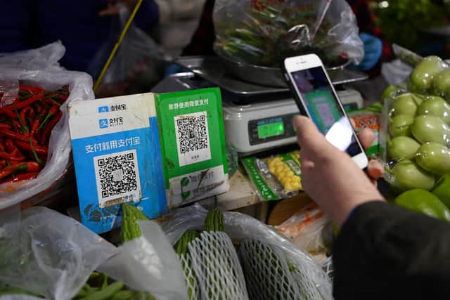 A customer makes a payment using a Wechat QR payment code (C) via her smartphone, next to an Alipay QR code (L), at a vegetable market in Beijing on November 3, 2020. (Photo by GREG BAKER/AFP via Getty Images)