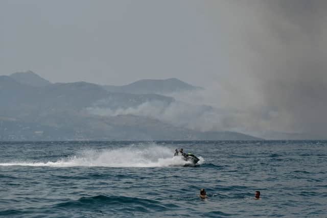 Beachgoers swim near the coastal town of Saranda as smoke billows from the Greek Island of Corfu (Photo: Getty Images)
