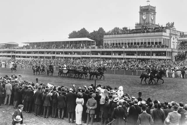 Spectators look on from the rail and grandstand King George V and Queen Mary in a horse drawn open landau carriage drive down the front stretch of the course on the opening day of the Royal Ascot race meeting on 16th June 1914 at the Ascot Racecourse in Ascot, Berkshire, England. (Photo by Central Press/Hulton Archive/Getty Images).