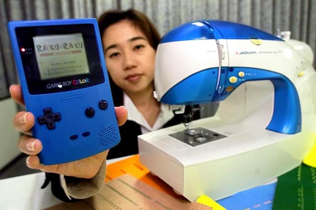 Naoko Haraguchi, employee of Japan's sewing machine maker Jaguar International Corporation, shows off its new home-use sewing machine "nu Eyell" (R) and a GAME BOY COLOR (L) of Nintendo Co., Ltd. in Tokyo 20 April 2000. The company developed a new computerized sewing machine controlled by a variety of sewing pattern data transferred from the portable game machine. (TORU YAMANAKA/AFP via Getty Images)