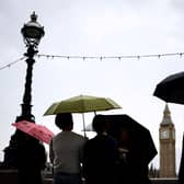 Pedestrians stand under umbrellas while looking at Elizabeth Tower, commonly called Big Ben, from the Southbank by the River Thames, in central London, on July 31, 2023 on a gloomy and rainy summer day.
