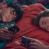 Joe Locke as Charlie Spring and Kit Connor as Nick Nelson in Heartstopper Series 2, both laying next to each other on their phones (Credit: Netflix) 