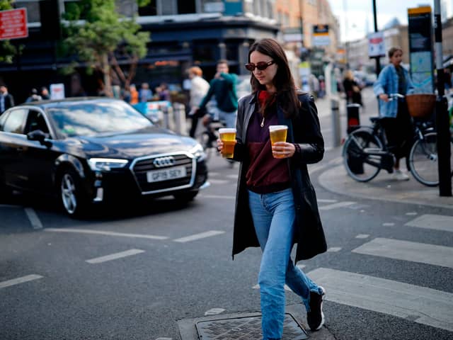 A woman carries takeaway draught beer in plastic cups from a pub in June 2020 (Photo: TOLGA AKMEN/AFP via Getty Images)