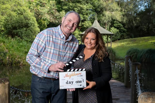 Alan Fletcher and Rebekah Elmaloglou behind the scenes filming Neighbours, holding a clapperboard that reads "day one" (Credit: Ray Messner)
