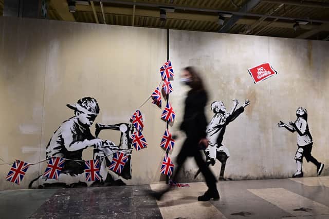 A visitor walks in fronf of a British street artist Banksy's murals "Slave Labour" (L) and "No Ball Games" (R) (Photo by MIGUEL MEDINA/AFP via Getty Images)
