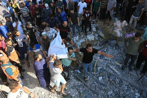 Palestinians rush with a body brought out from under a collapsed building following an Israeli airstrike in Rafah, in the southern part of Gaza Strip, on October 16, 2023. (Photo by SAID KHATIB/AFP via Getty Images)