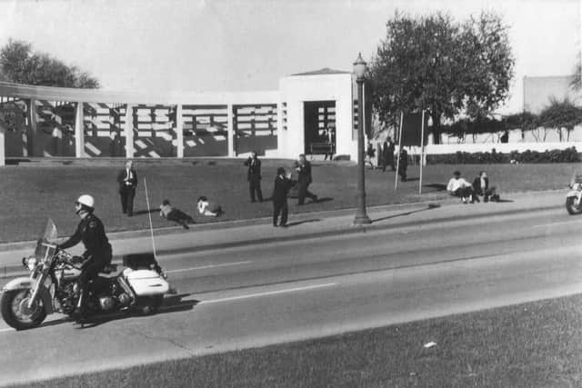 Assassination of JFK aftermath at Dealey Plaza; The Umbrella Man is sitting next to the road sign (the man on the right side) (Credit: Public Domain)