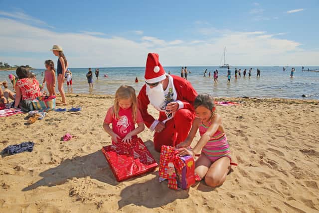 Santa Claus helps children to open their Christmas presents on Christmas Day at Brighton Beach on December 25, 2013 in Melbourne, Australia (Scott Barbour/Getty Images)