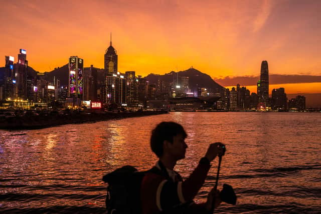A man takes picture at East Coast Park Precinct as city's skyline is seen during the dusk in Hong Kong on December 20, 2022. (Photo by Philip FONG / AFP)