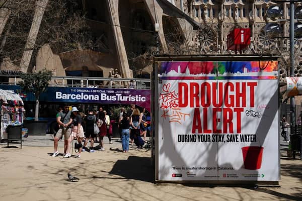 A couple uses a selfie stick to take a picture next to a banner warning tourists on drought alert in Catalonia (Photo: PAU BARRENA/AFP via Getty Images)