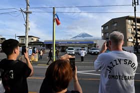 This photo taken on May 20, 2024 shows tourists taking pictures of Mount Fuji from opposite a convenience store in the town of Fujikawaguchiko, Yamanashi prefecture. (Photo by Kazuhiro NOGI / AFP) (Photo by KAZUHIRO NOGI/AFP via Getty Images)