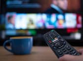 Netflix remote control with TV behind in evening with Netflix menu (Shutterstock)