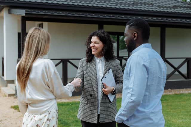 Three people standing outside, two are shaking hands.