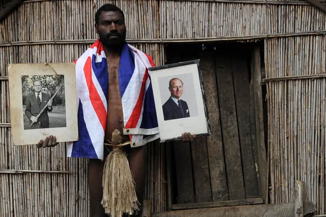Sikor Natuan, the son of the local chief, holds two official portraits (one holding a pig-killing club, L) of Britain's Prince Philip in front of the chief's hut in the remote village of Yaohnanen on Tanna in Vanuatu on August 6, 2010. (Photo: TORSTEN BLACKWOOD/AFP via Getty Images)