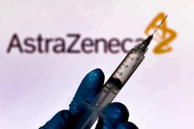 A medical syringe is seen with AstraZeneca company logo displayed on a screen in the background