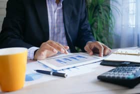 A business professional analyzes financial data on a digital tablet, surrounded by charts, a notebook, and a calculator, highlighting a focused work environment.
