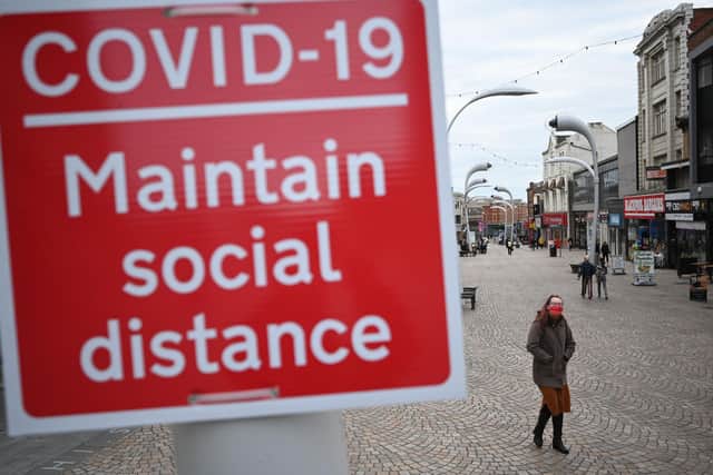 A woman wearing a face mask walks by a sign encouraging social distancing in a street in Blackpool, Lancashire (Photo by OLI SCARFF/AFP via Getty Images)
