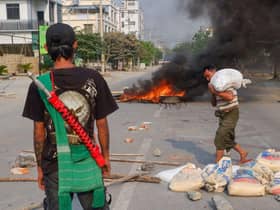 A man carries a sandbag to erect a barricade, as another burns in the distance, as security forces staged a crackdown on demonstrations against the military coup, in Mandalay on 22 March (Picture: Getty Images)